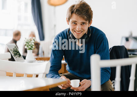 Ritratto di uomo sorridente in un cafe che indossano le cuffie Foto Stock