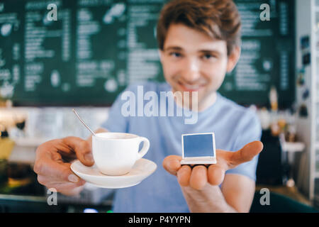 Uomo sorridente in un bar che offre caffè e tenendo in miniatura modello di computer portatile Foto Stock