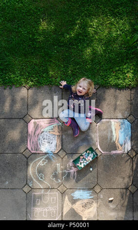 Sorridente bambina disegno con chalk all'aperto, vista dall'alto Foto Stock