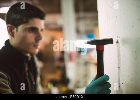 L'uomo martellare un grano in una parete Foto Stock