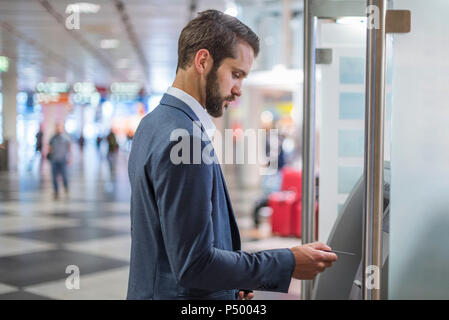 Giovane imprenditore il ritiro di denaro presso un bancomat in città Foto Stock