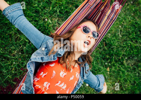 Ritratto di cantare ragazza indossando occhiali da sole giacente in amaca Foto Stock