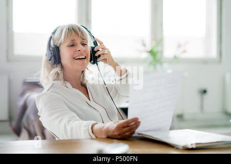 Ridendo imprenditrice maturo che indossano le cuffie guardando il documento alla scrivania Foto Stock