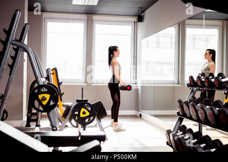 La donna il sollevamento pesi in palestra cercando in specchio Foto Stock