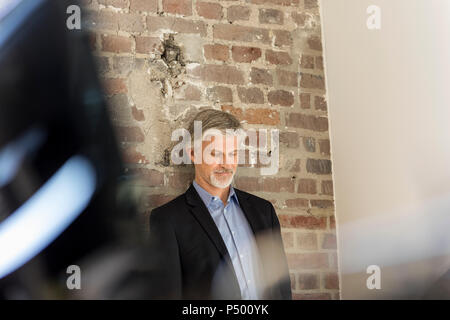 Imprenditore maturo appoggiato su di un muro di mattoni in office Foto Stock