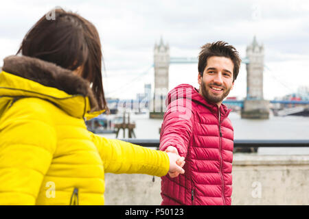 UK, Londra, Ritratto di giovane sorridente man standing mano nella mano sul ponte sul Tamigi con la sua ragazza Foto Stock