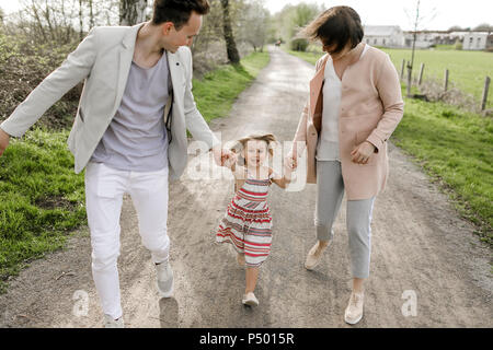 Bambina tenendo le mani dei genitori mentre è in esecuzione Foto Stock