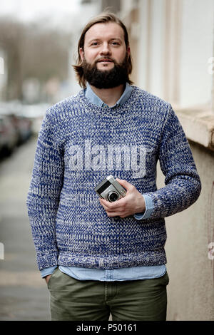 Uomo con la barba in piedi in strada, tenendo vecchia macchina fotografica Foto Stock