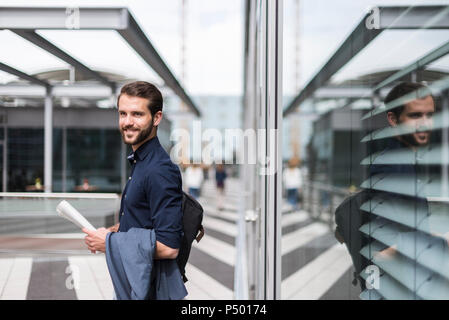 Sorridente giovane imprenditore all'aperto permanente tenendo giornale Foto Stock