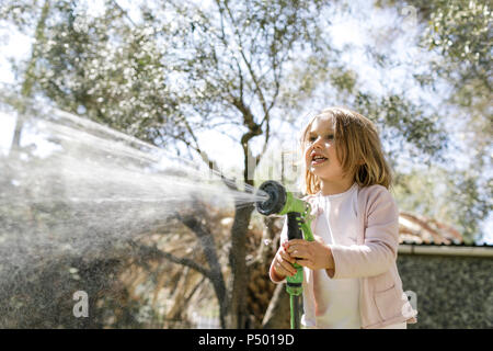 Sorridente bambina gioca con tubo flessibile da giardino Foto Stock