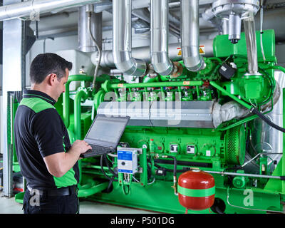 Impianto di cogenerazione di energia termica ed elettrica, lavoratore utilizzando laptop nella parte anteriore del motore a gas Foto Stock