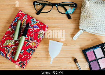 Coppa mestruale su un tavolo e notebook, penna e occhiali Foto Stock