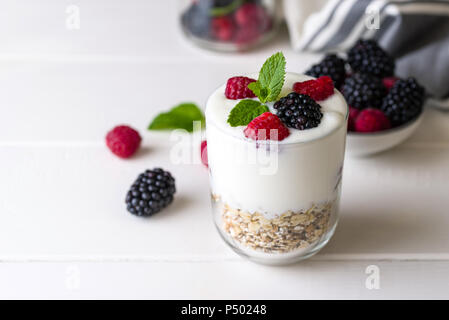 Yogurt bianco con muesli e lamponi in recipiente di vetro bianco su sfondo di legno. Foto Stock