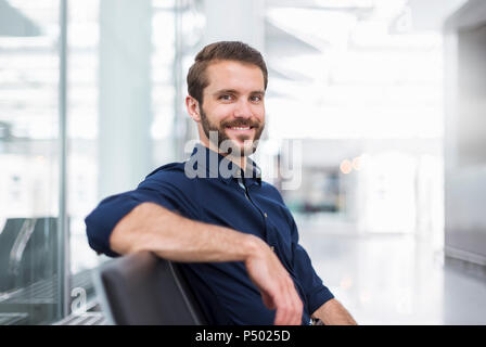 Ritratto di giovane sorridente imprenditore seduto in area di attesa Foto Stock