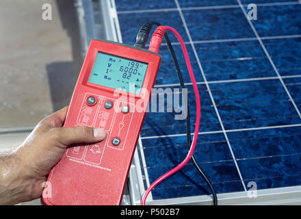 Mano d'uomo di contenimento del dispositivo di misurazione di fronte impianto solare, close-up Foto Stock
