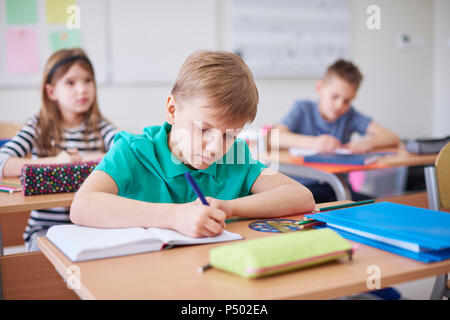 Scolaro iscritto nel libro di esercizi in classe Foto Stock