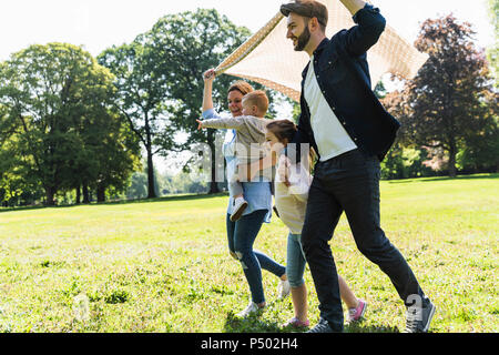 La famiglia felice a piedi con una coperta in un parco Foto Stock