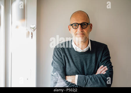 Ritratto di un uomo anziano, staning davanti al muro con le braccia incrociate Foto Stock