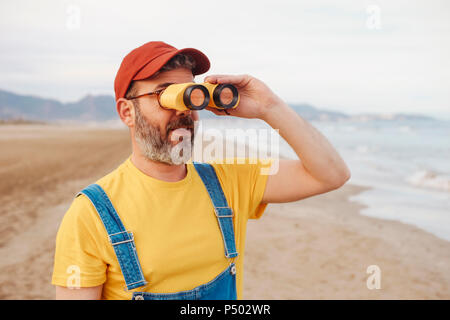 Uomo Barbuto con il binocolo sulla spiaggia Foto Stock