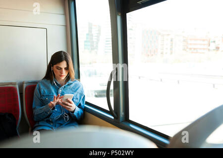 Giovane donna seduta in bus ascoltando musica con il telefono cellulare e gli auricolari Foto Stock