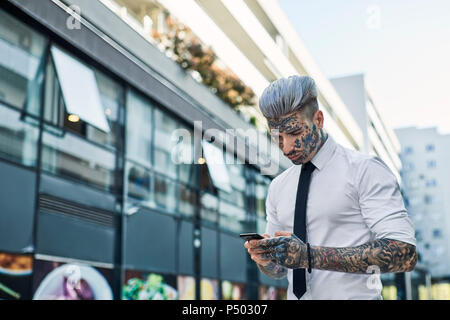 Giovane imprenditore con tatuato faccia utilizza lo smartphone Foto Stock