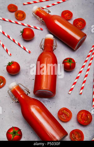 In casa di succo di pomodoro in swing top bottiglie, cannucce e pomodori sul terreno grigio Foto Stock