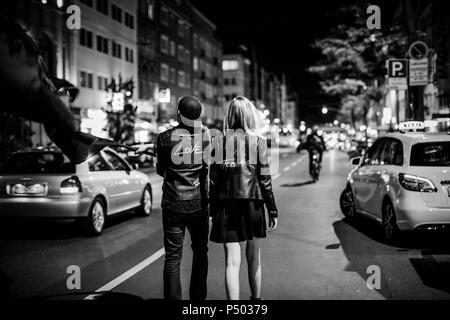 Vista posteriore della giovane coppia con bandiera nera a camminare per strada di notte Foto Stock