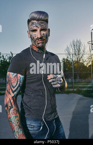 Ritratto di tatuati giovane uomo che ascolta la musica con gli auricolari Foto Stock