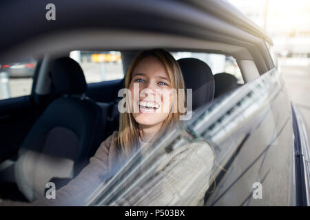 Ritratto di ridere giovane donna seduta in auto Foto Stock