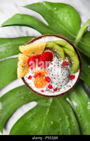 Ciotola di noce di cocco con vario frutta, yogurt naturale e semi sulla foglia Foto Stock