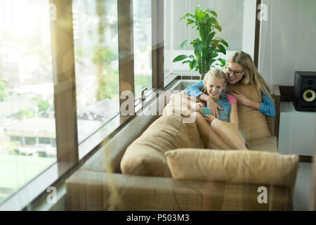 Madre e figlia in soggiorno moderno su un divano guardando insieme allo smartphone Foto Stock