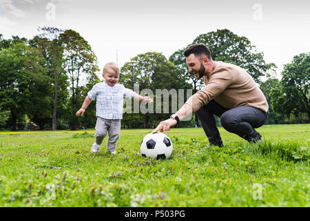 Padre Felice giocando a calcio con il figlio in un parco Foto Stock