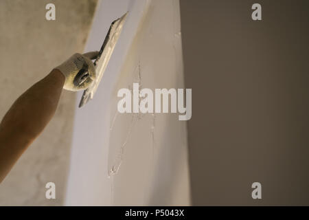 Lavoratore di applicare lo stucco sulla parete con il coltello da stucco, fondale focus Foto Stock