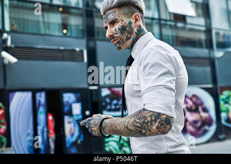 Giovane imprenditore con tatuato faccia utilizza lo smartphone Foto Stock