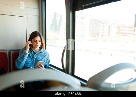 Giovane donna seduta in bus ascoltando musica con il telefono cellulare e gli auricolari Foto Stock