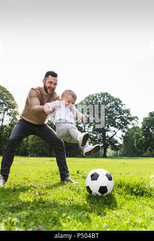 Padre Felice giocando a calcio con il figlio in un parco Foto Stock