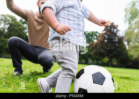 Padre Felice giocando a calcio con il figlio in un parco Foto Stock
