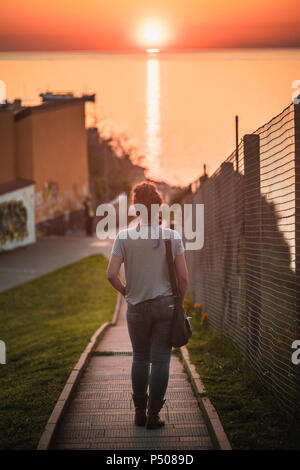 Un giovane viandante cammina verso il tramonto sul mare dopo una giornata di esplorazione. Foto Stock