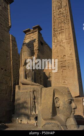 L'Egitto. Tempio di Luxor. Vista parziale del primo pilone del tempio e i resti di un obelisco di granito rosa e la testa e colossali statue di Ramses II. Antica Tebe "Waset,. Foto Stock