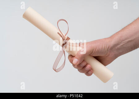 Un diploma arrotolato e legato con un nastro rosso per la mano Foto Stock