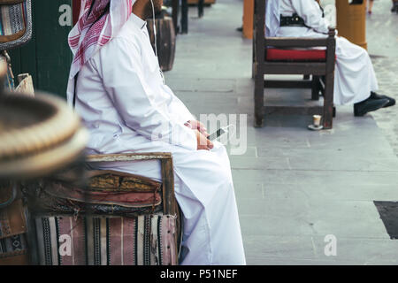 Arab giovane uomo che ascolta musica sul suo telefono su strada. Souq Waqif street a Doha, in Qatar. Non riesco a vedere il volto. Foto Stock