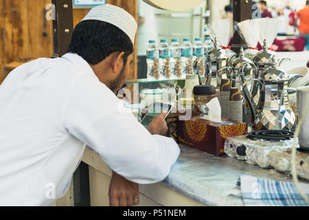 Doha, Qatar - Mart 2018: giovane uomo arabo facendo qualcosa sul suo telefono cellulare mentre si lavora su strada stand di caffè a Doha. Souq Waqif street. Foto Stock