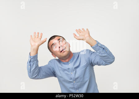 Ritratto di giovane uomo caucasico in maglietta blu sollevando in alto le mani come se difendere da qualcosa che cade, esprimendo sorpresa e leale, sensazione di pericolo ov Foto Stock