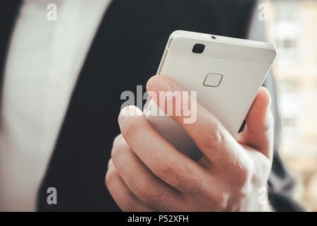 Una macro di un imprenditore che utilizzano uno smartphone di fronte a uno sfondo luminoso Foto Stock