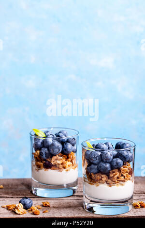 Mirtillo dessert, cheesecake, inezia, muesli in un vetro su di un legno tavolo vintage con crepe. Foto Stock