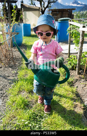 Ragazza giovane che porta un grande verde annaffiatoio come lei aiuta nel giardino vegetale Foto Stock