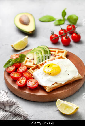 Una sana prima colazione. cialde belghe con avocado, Uovo fritto, pomodori ciliegia su un cemento grigio Sfondo. vista da sopra Foto Stock