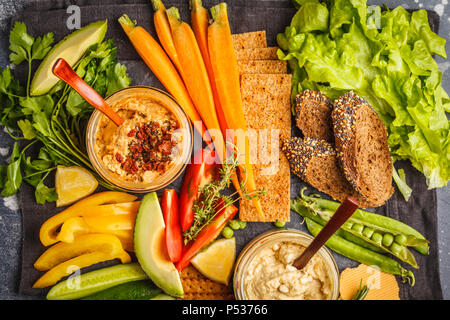 Vegetariano dip arabo hummus con verdure e stuzzichini vari su uno sfondo scuro. Sano cibo vegan concetto. Foto Stock