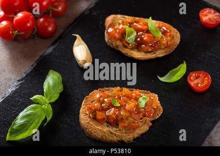 Freschi Fatti in casa italiana croccante antipasto chiamato Bruschetta condito con pomodoro, aglio, pepe rosso e basilico Foto Stock