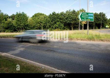 Cattiva strada su superfici di le strade della Gran Bretagna. Giunzione di Pyebush rotonda e A355, Beaconsfield. Rivolta verso il filo di acciaio inossidabile. Vettura in movimento. Foto Stock